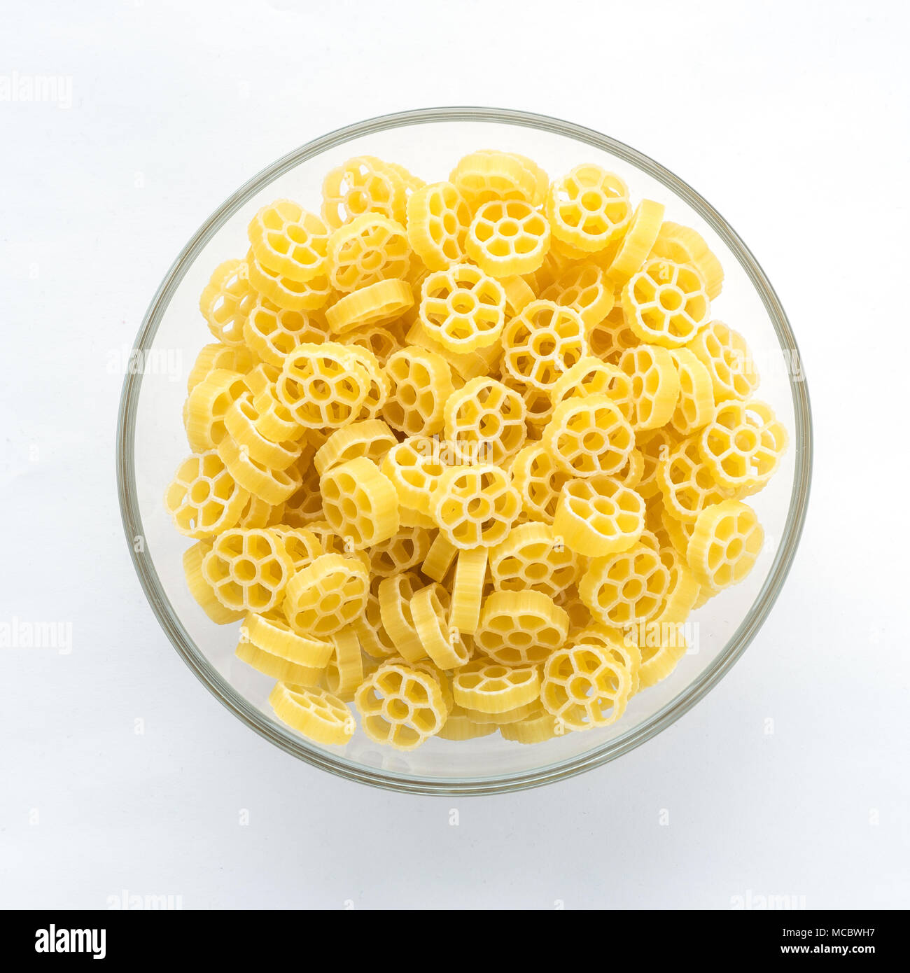 Macaroni ruote pasta in glass bowl on white isolated background, in the center close-up with top. Stock Photo