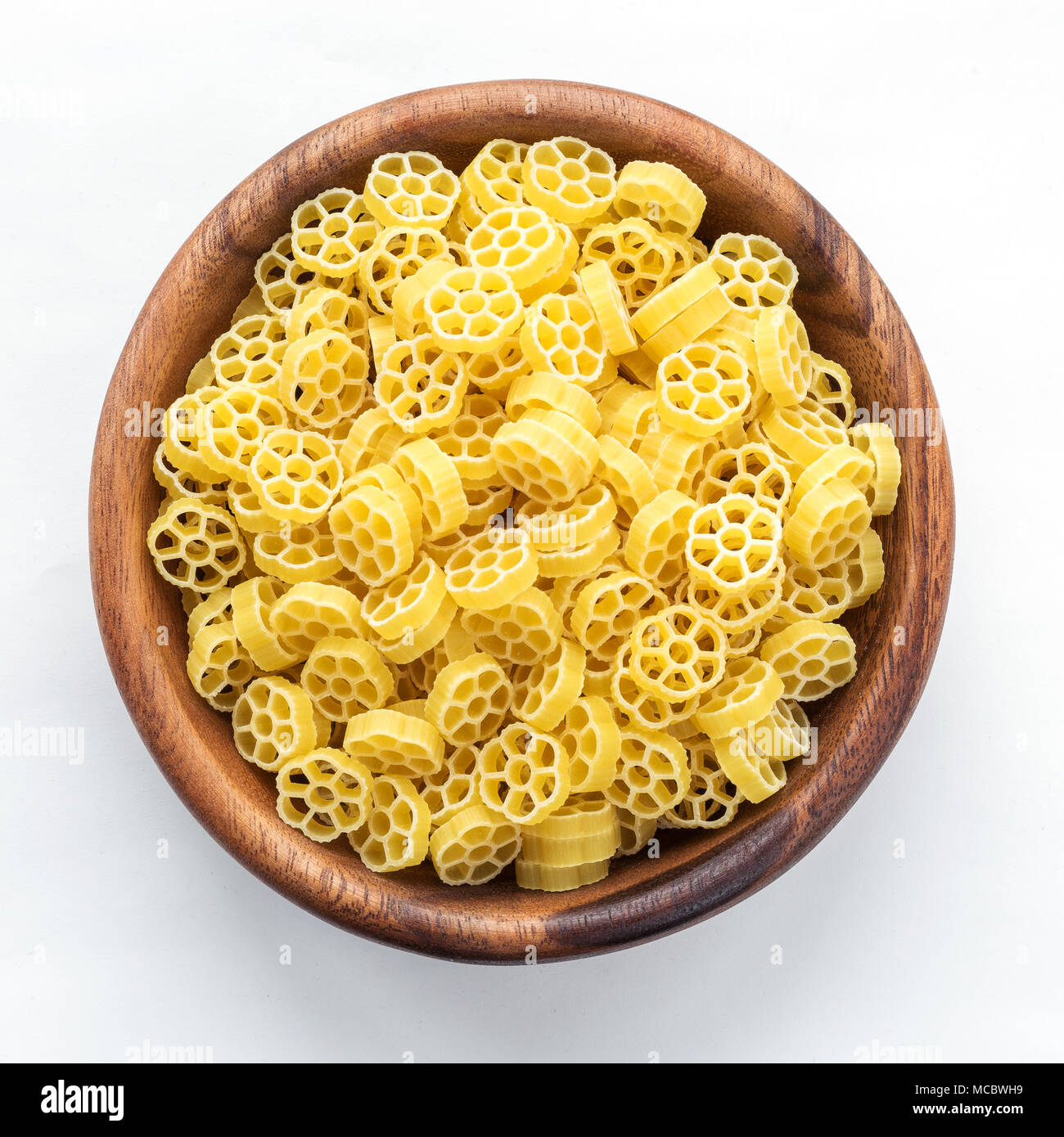 Macaroni ruote pasta in wooden bowl on white isolated background, in the center close-up with top. Stock Photo
