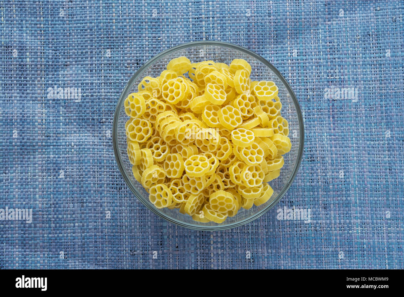 Macaroni ruote Pasta in a glass bowl on a blue knitted background in the center. Close-up with the top. Stock Photo