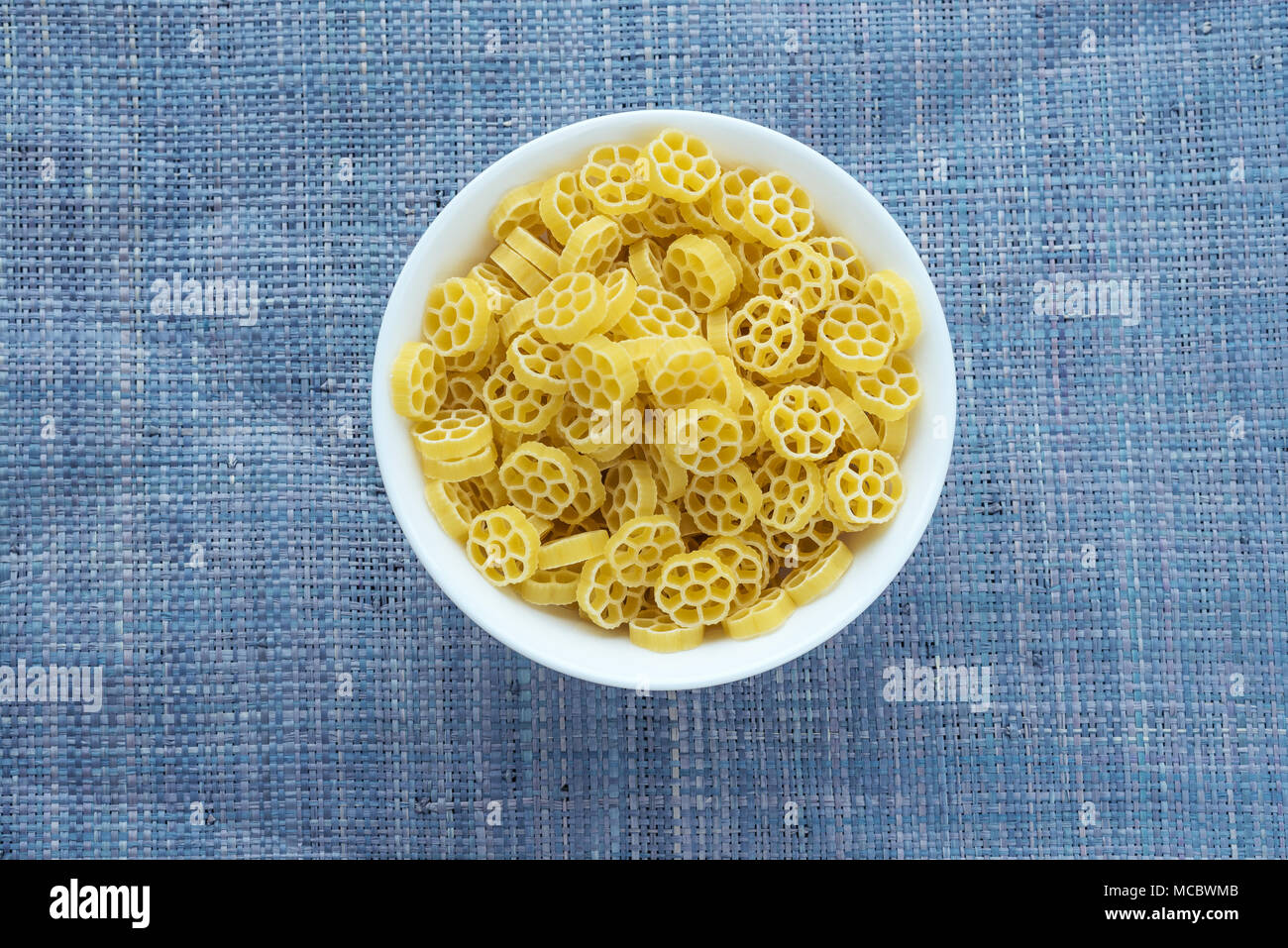 Macaroni ruote Pasta in a white cup on a blue knitted background in the center. Close-up with the top. Stock Photo