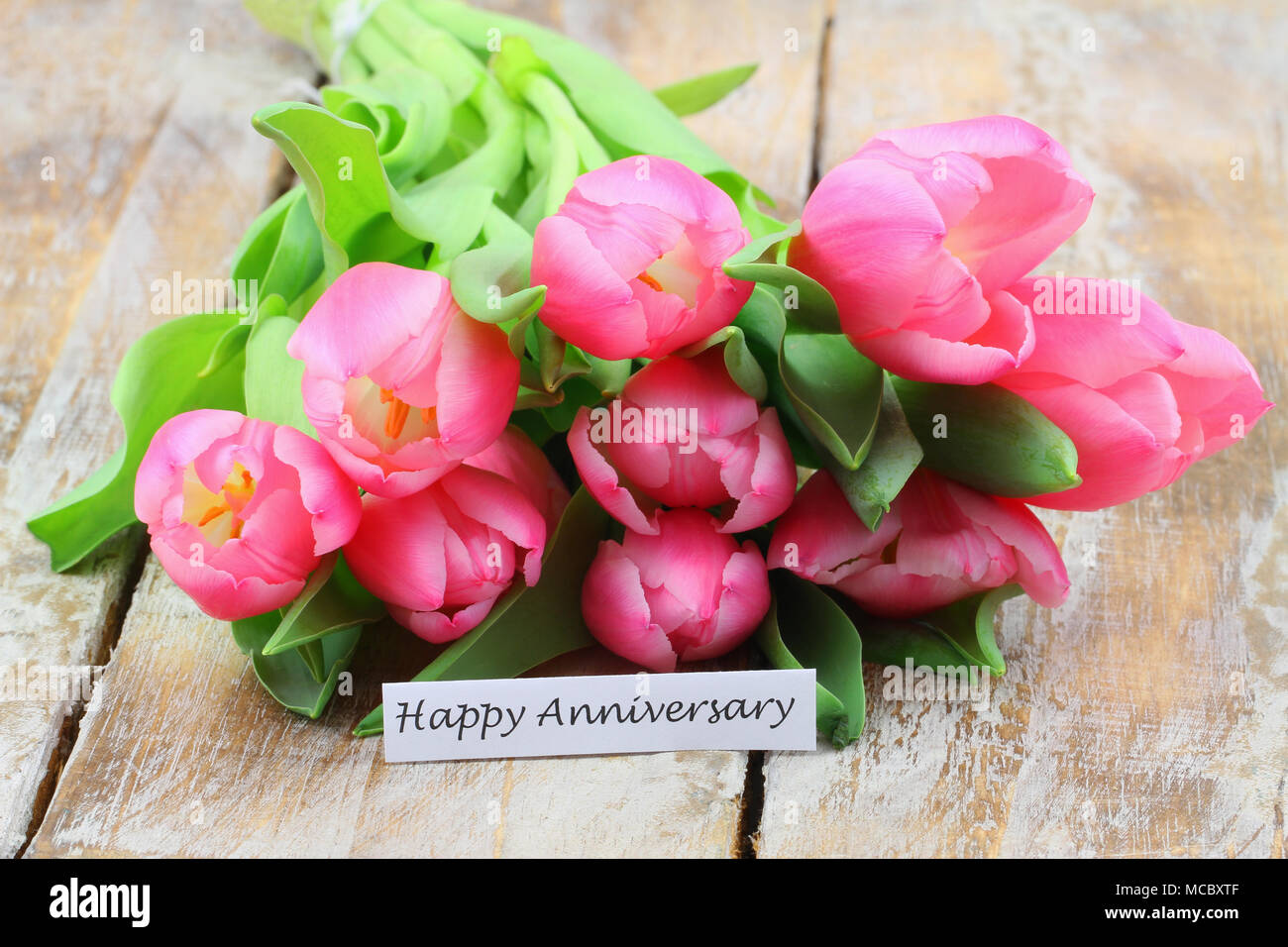 Happy Anniversary card with pink tulip bouquet on wooden surface Stock ...