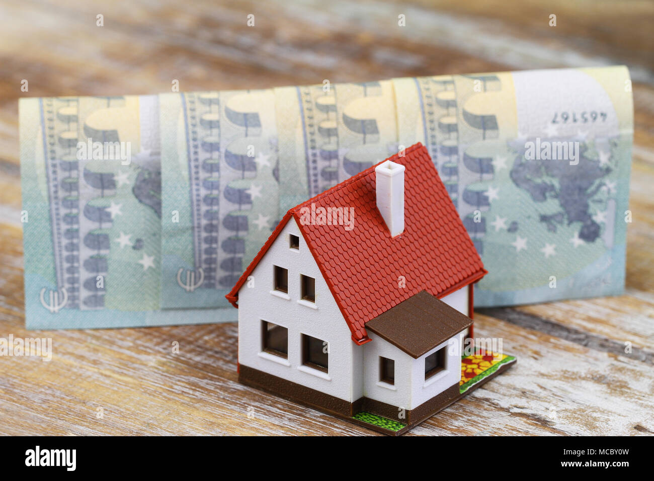 Model house in front of folded Euro banknotes on wooden surface Stock Photo