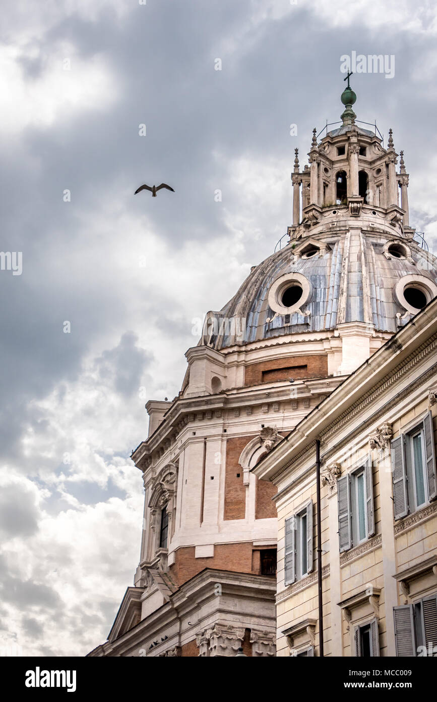 16th century church dome of Santa Maria di Loreto in Rome, beside building with shutters, bird flying against cloudy gray sky. Stock Photo