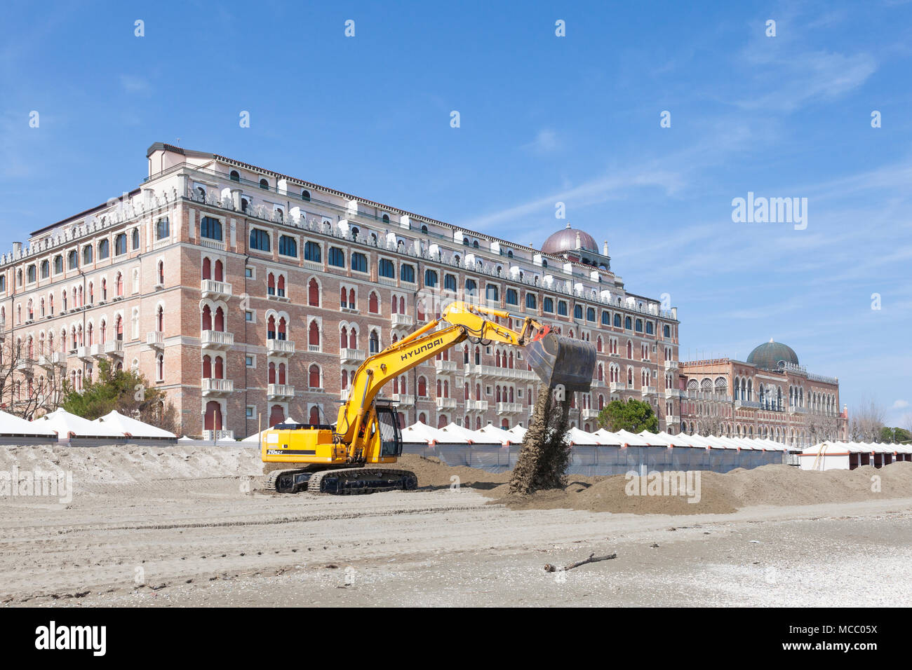 Excavator  or digger preparing the beach for summer in front of the Excelsior Hotel, Lido di Venezia (Venice Lido), Venice, Veneto, Italy moving piles Stock Photo