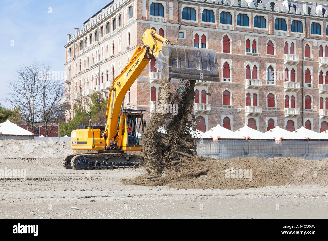 Excavator preparing the beach for summer tourism, Lido di Venezia, (Venice Lido, Lido Island) ), Venice, Veneto, Italy in front of the luxury Excelsio Stock Photo