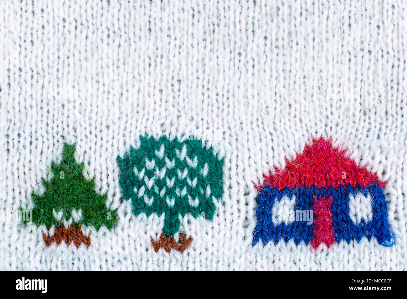 Knitted house with trees on white knitted background. Stock Photo