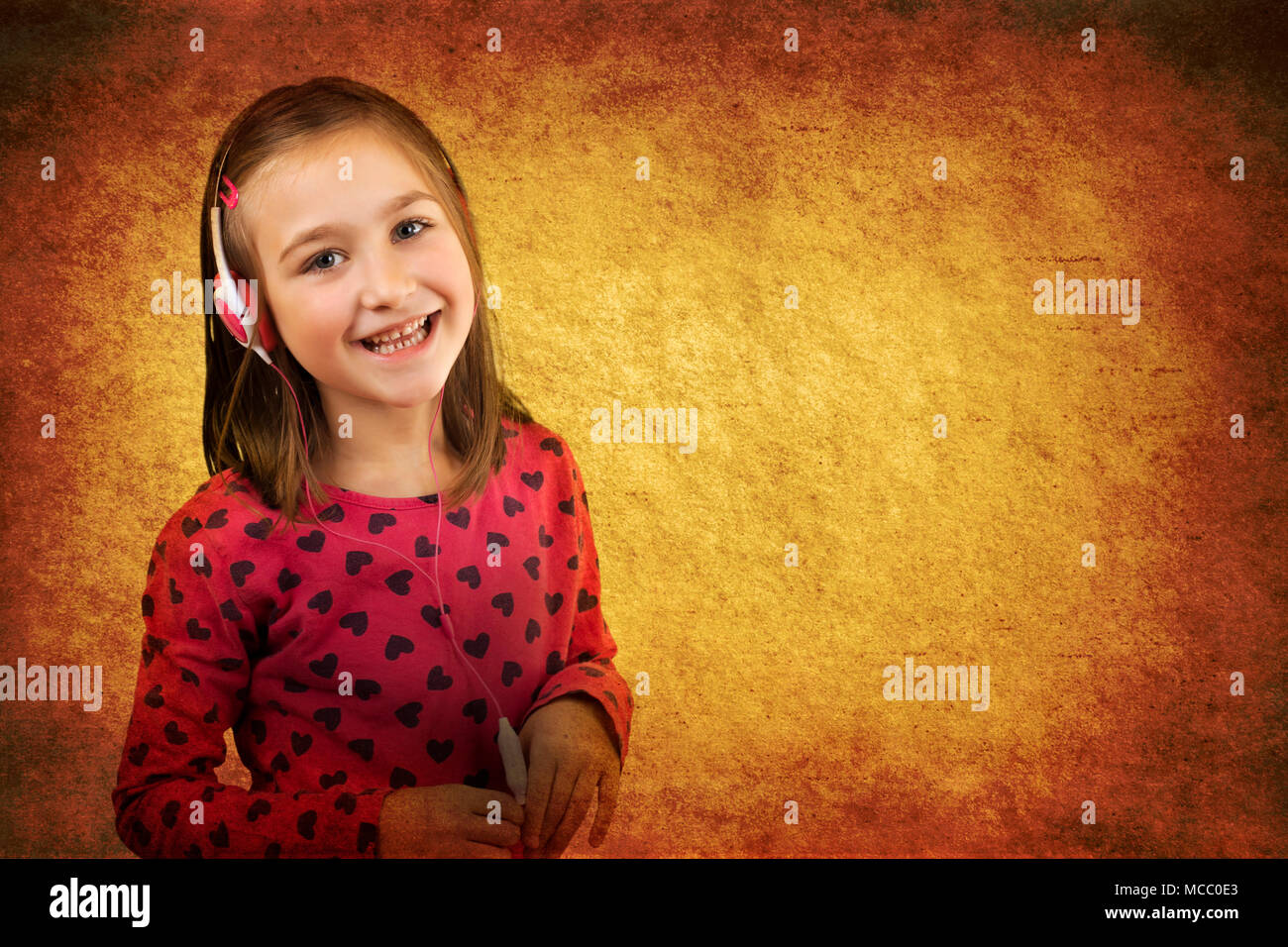 Little happy girl with headphones having fun listening to the music. Vintage grunge paper background. Stock Photo