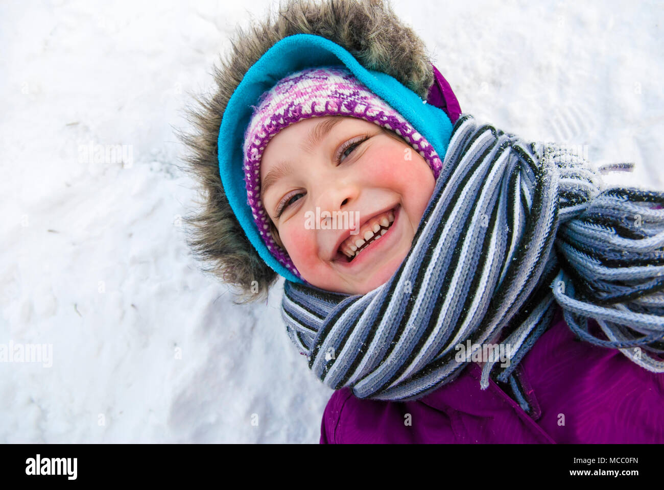 Happy little girl laying in snow with big smile. Stock Photo