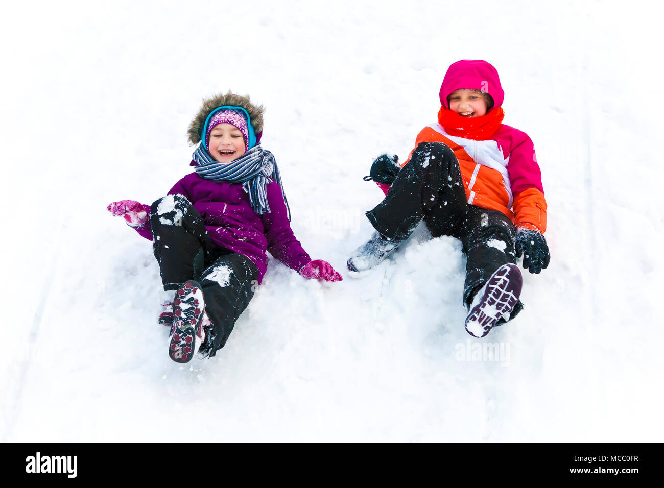 Two sisters having fun together while sliding downhill at winter time. Stock Photo
