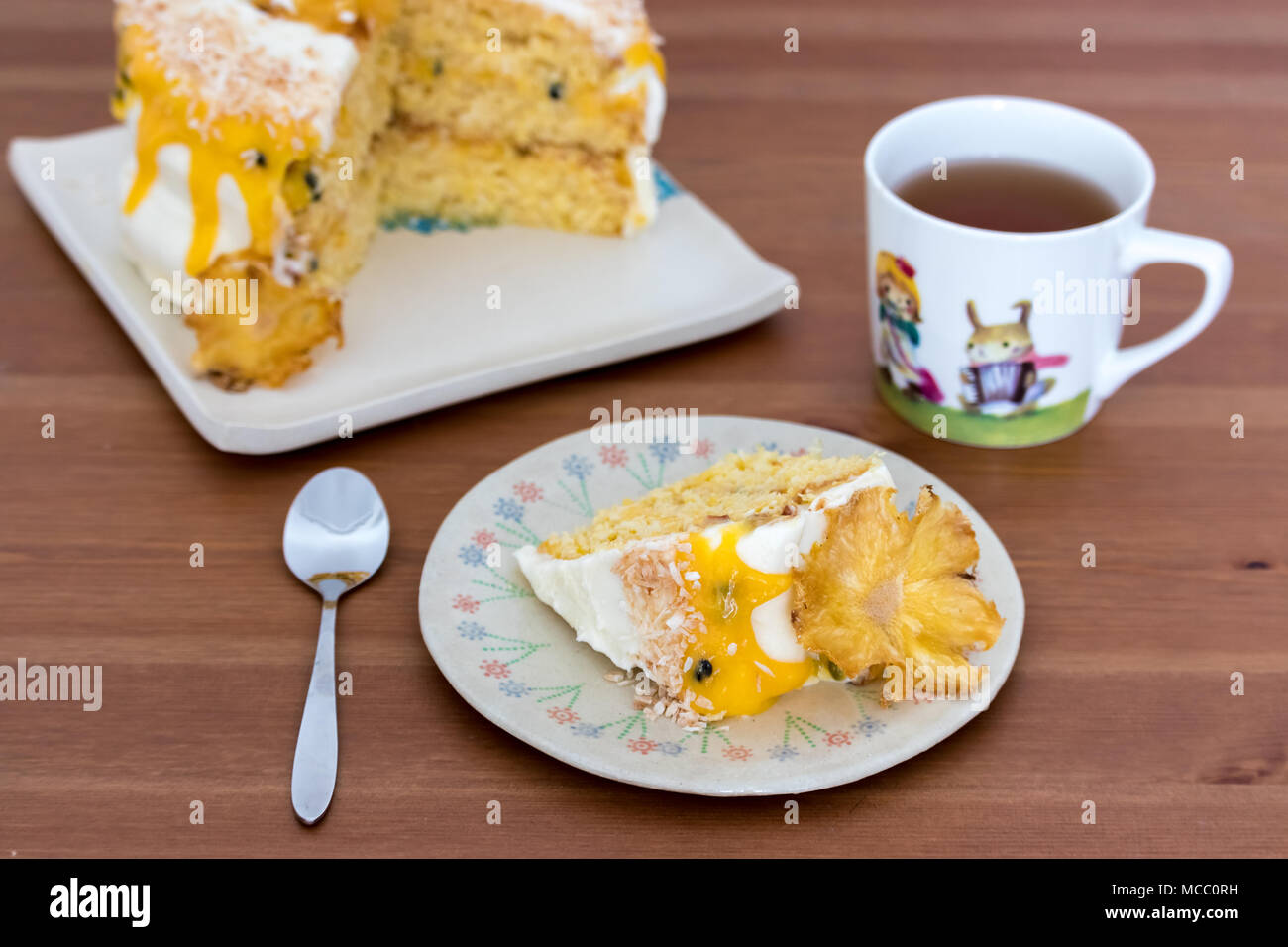 A slice of pineapple and coconut cake with passion fruit curd, served on handmade plate with black tea. Stock Photo