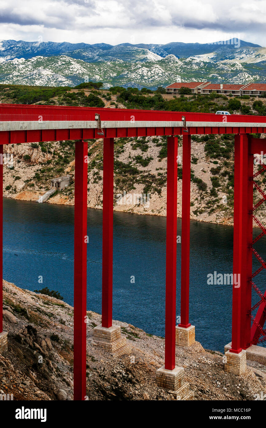 The red painted Maslenica deck bridge spanning the Novsko Zdrilo strait of the Adriatic Sea with Croatian landscape of houses and the Dinaric Alps Stock Photo