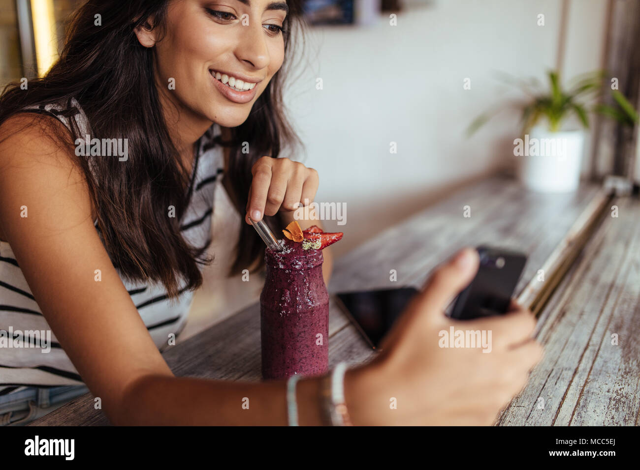 Woman taking a selfie with a smoothie using a mobile phone for her food blog. Food blogger shooting photos for her blog at home. Stock Photo