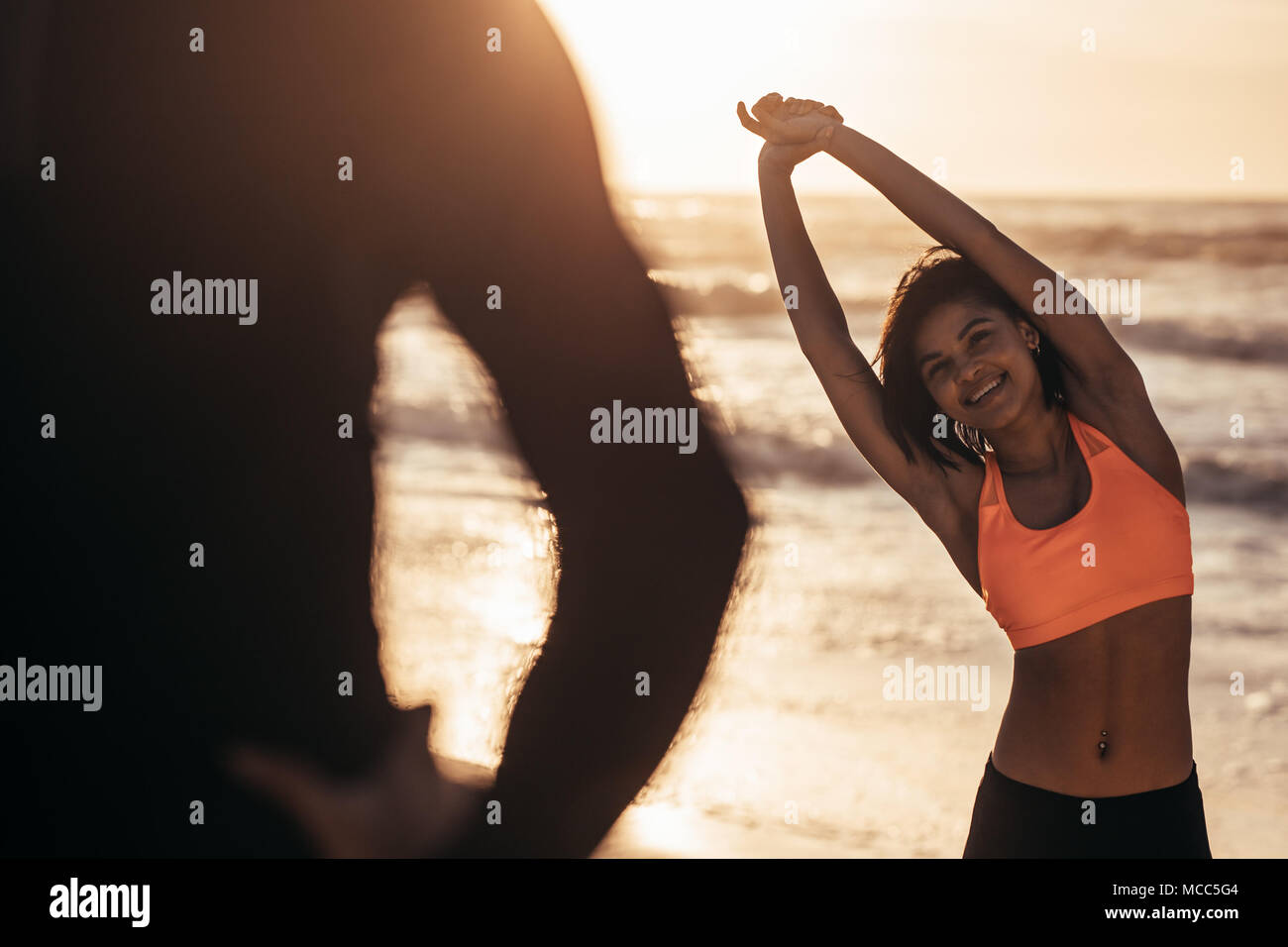 Woman in sportswear exercising at the beach with her trainer. Athletic woman working out at the beach in morning. Stock Photo