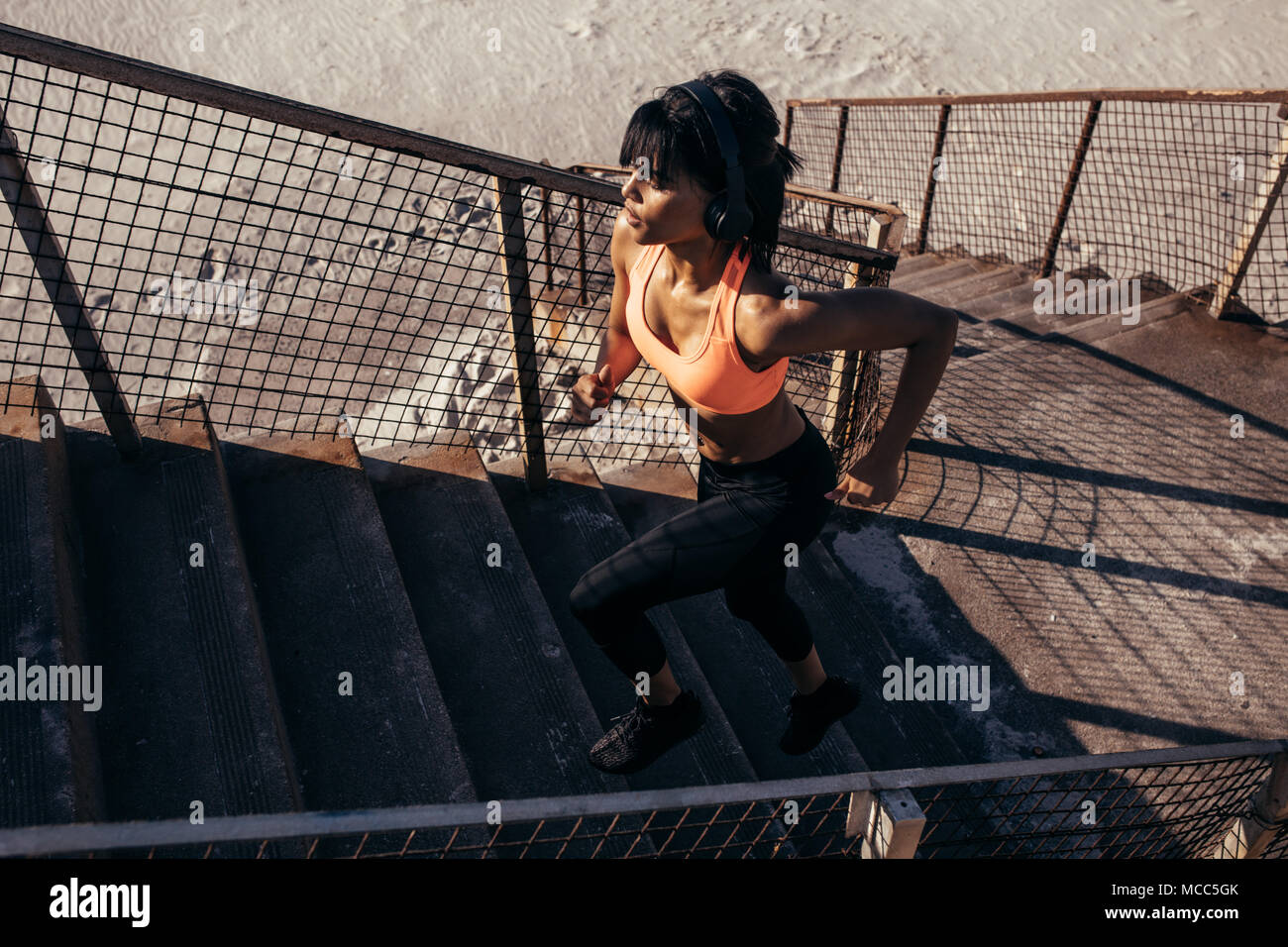 fitness woman running up the stairway along the beach. Female athlete exercising outdoors in morning. Stock Photo
