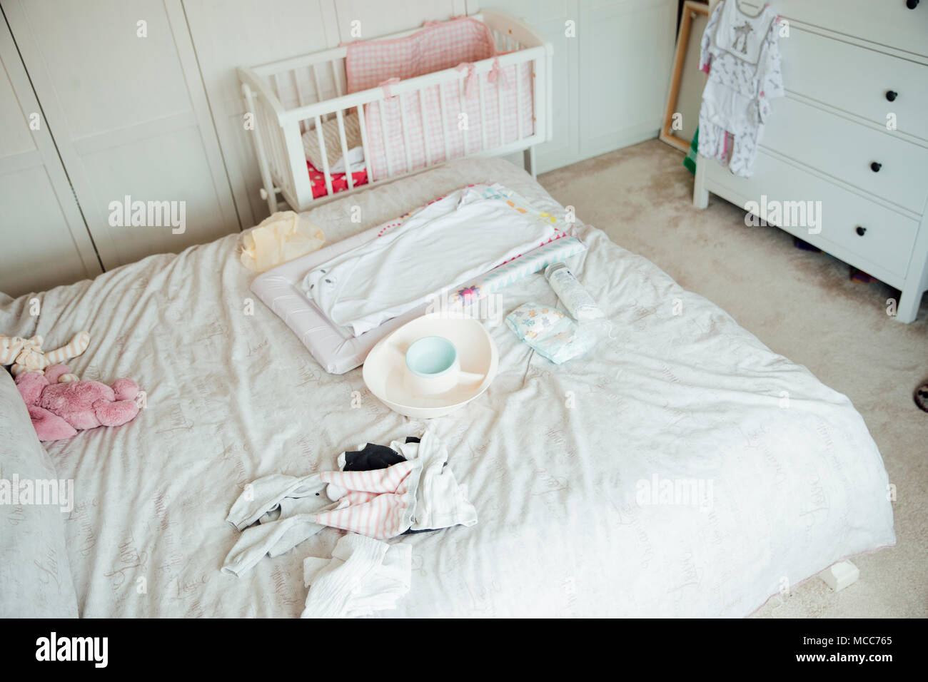A mother's bedroom is filled with baby equipment. There is a changing mat and clothes sprawled over the bed. Stock Photo