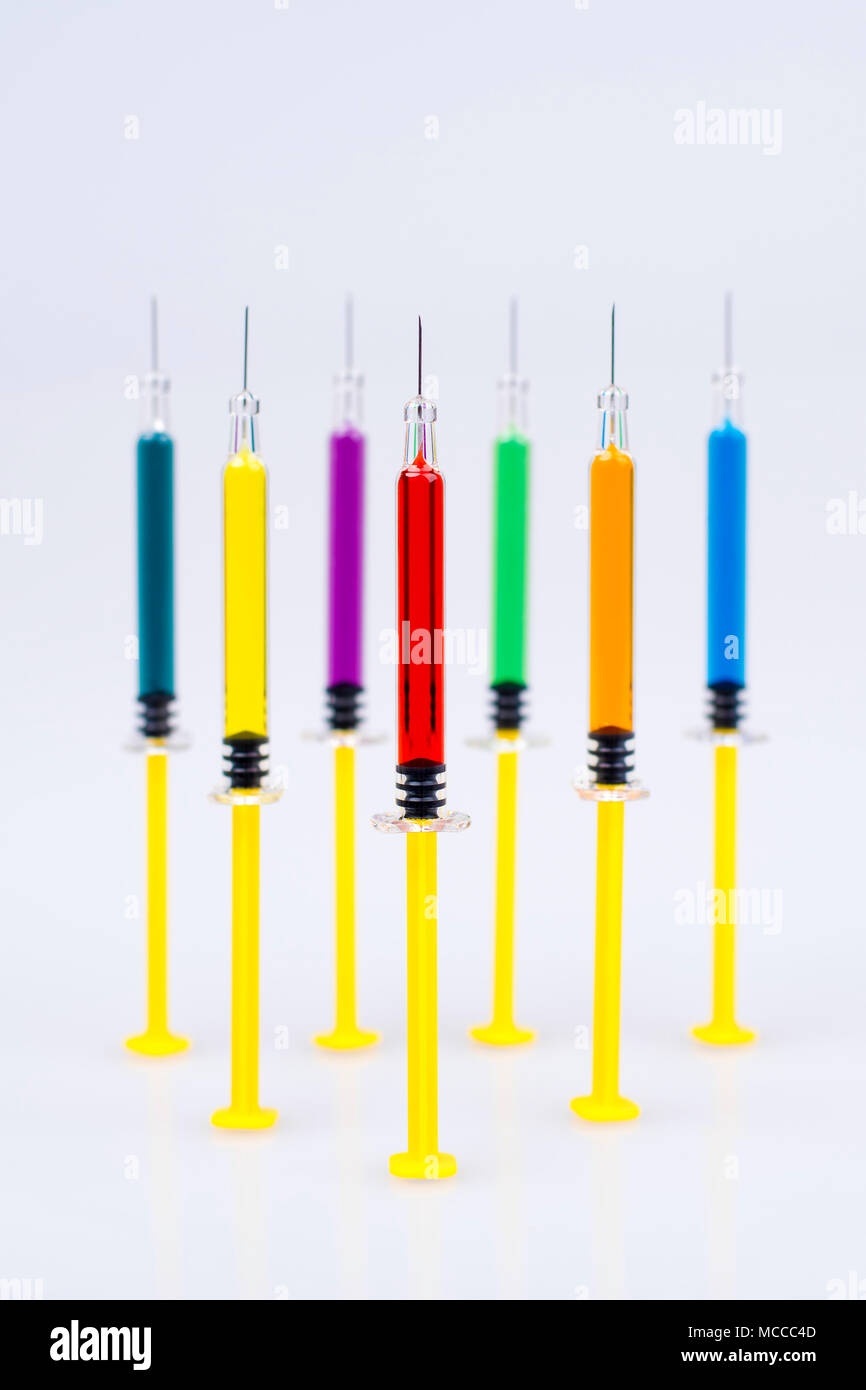 Multiple syringes with needles, filled with various colours of medicine/vaccines. Stock Photo