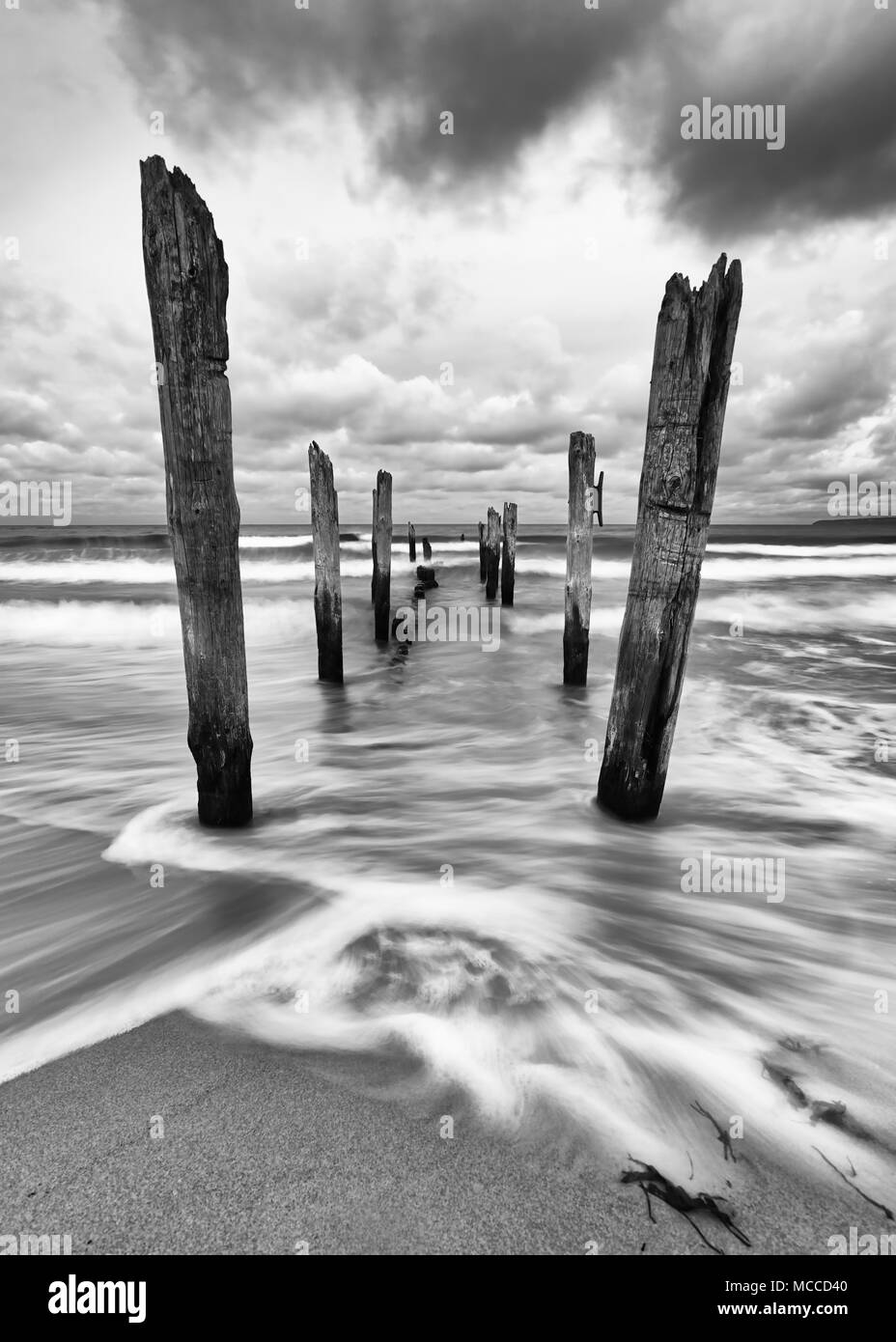 Scenic view of wooden poles on a beach, the movement of the waves is shown in addition to a colorful evening sky, black and white version Stock Photo