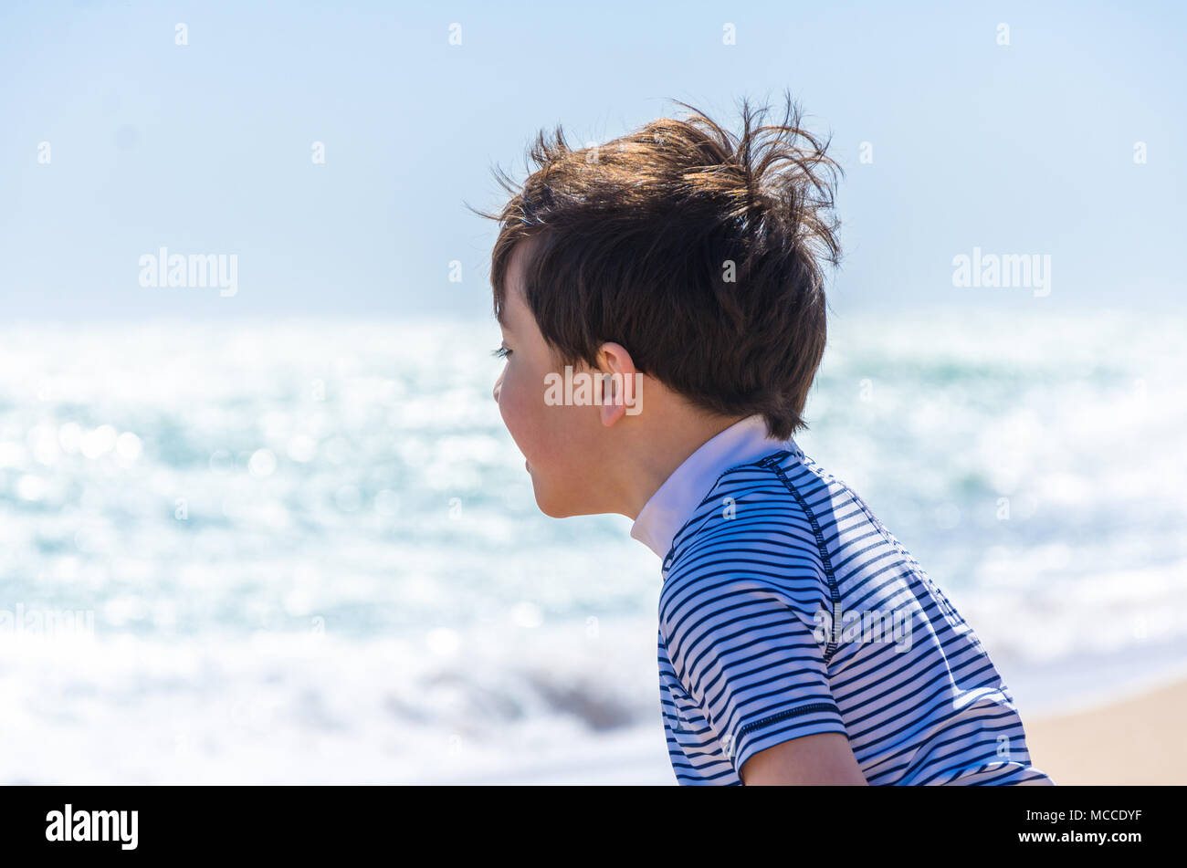 A young child plays on a beach close to the waves which roll in on the sand. Stock Photo