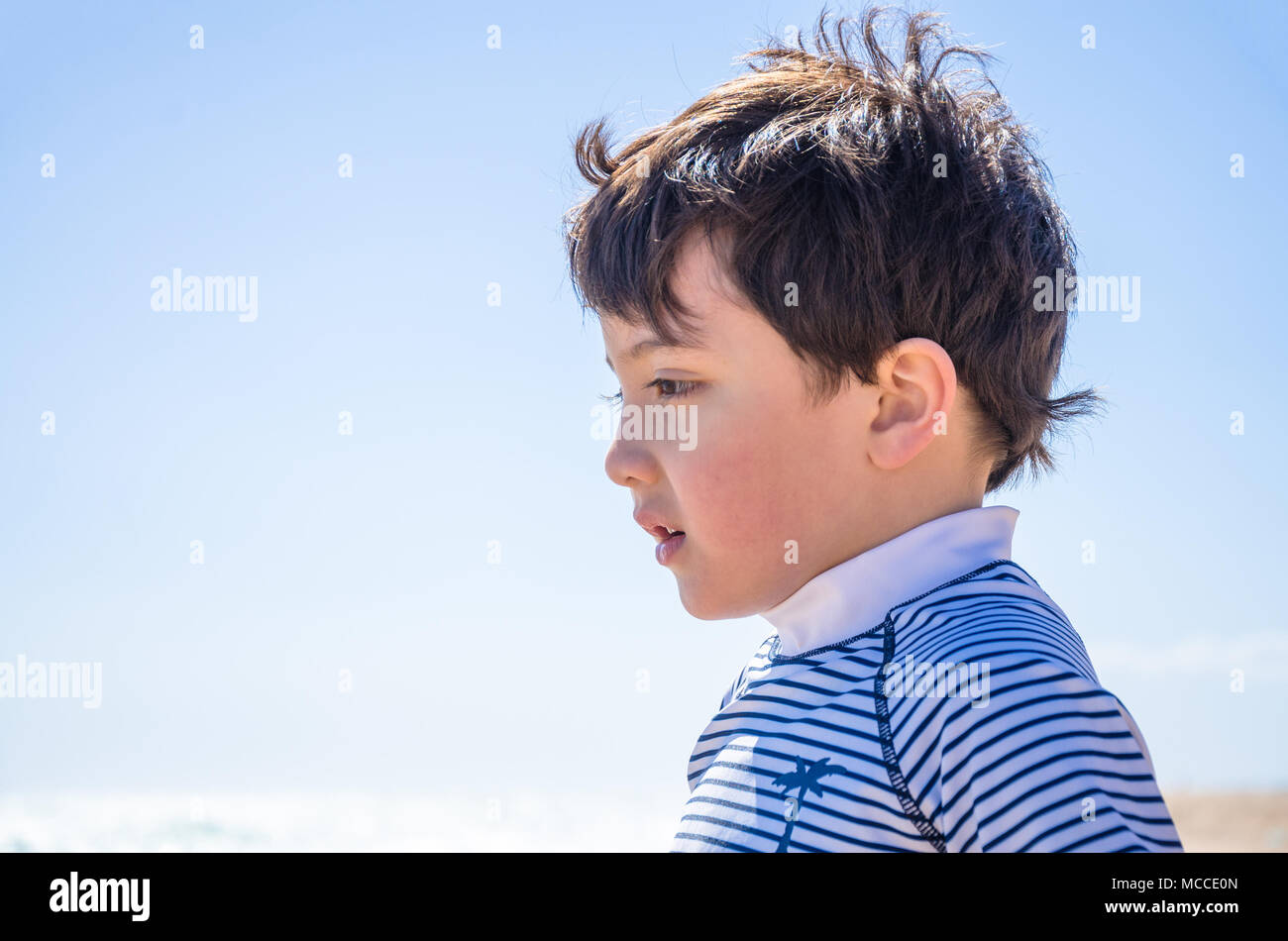 A portrait of a young boy taken outside against a clear blue sky while ...