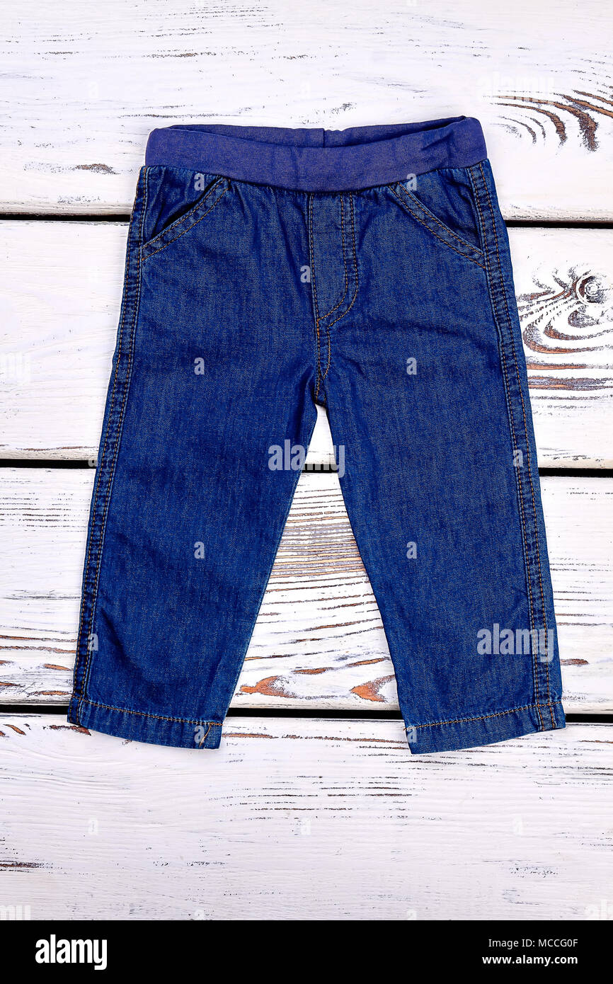 Babyboy denim trousers. Infant boy dark blue jeans on white wooden