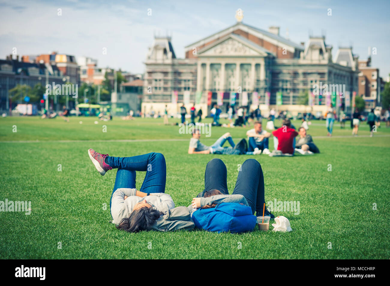 Relaxed couple on grass in public park with the VanGogh museum on the background, Amsterdam, Holland Stock Photo