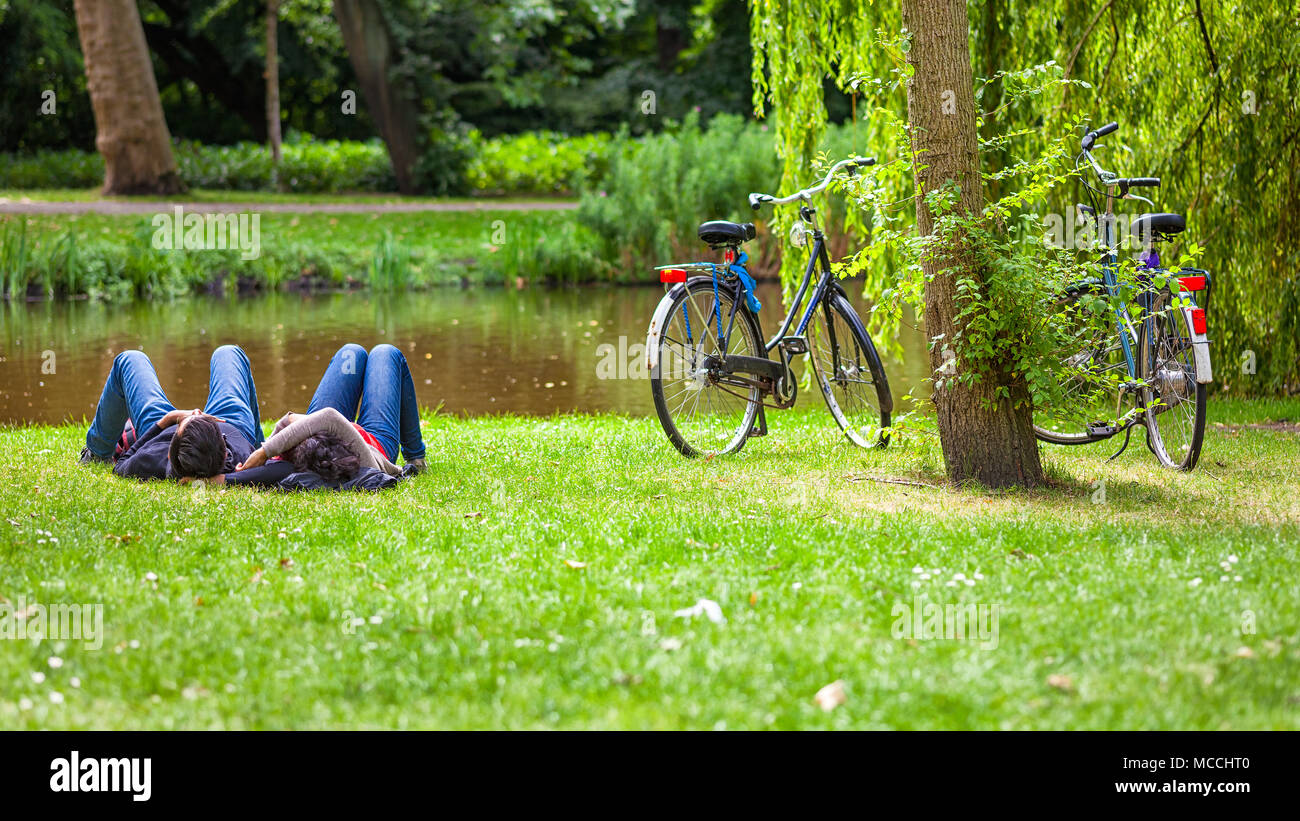 Relaxed couple on grass in public park after a bike riding, Vondelpark, Amsterdam, Holland Stock Photo