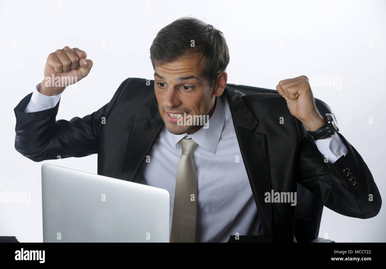 Young stressed handsome businessman working at desk in modern office shouting at laptop screen and being angry about financial situation, jealous of r Stock Photo