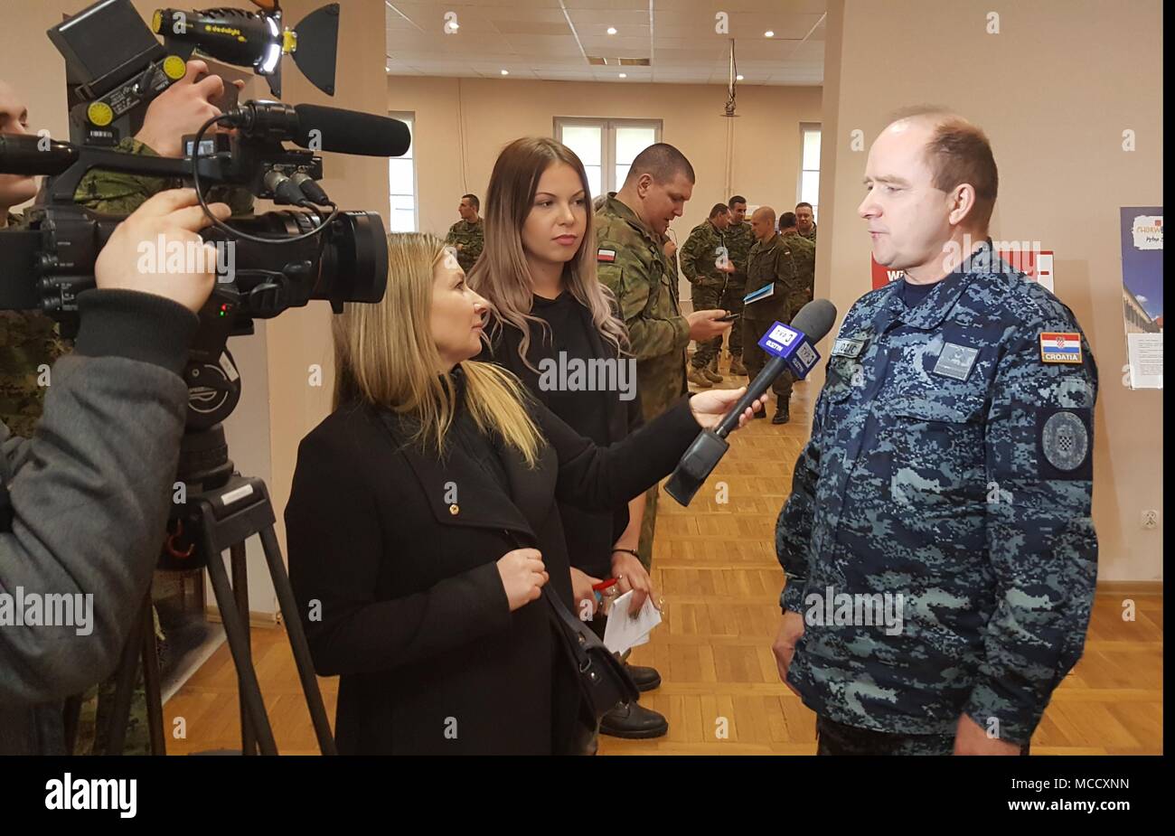 Croatian Navy Capt. Jozić, military attaché to Poland, conducts an interview with Polish media TVP3 explaining the Croatian cultural heritage events, Sylwia Pindor (center) serves as linguist during the interview at the Polish 15th Mechanized Brigade headquarters at Giżycko, Poland, Feb. 12, 2018. The celebration allowed the ambassador to express gratitude to Polish leaders and shared Croatian culture with the community leaders in attendance. The unique, multinational battle group is comprised of U.S., U.K., Croatian and Romanian soldiers serve with the Polish 15th Mechanized Brigade as a dete Stock Photo