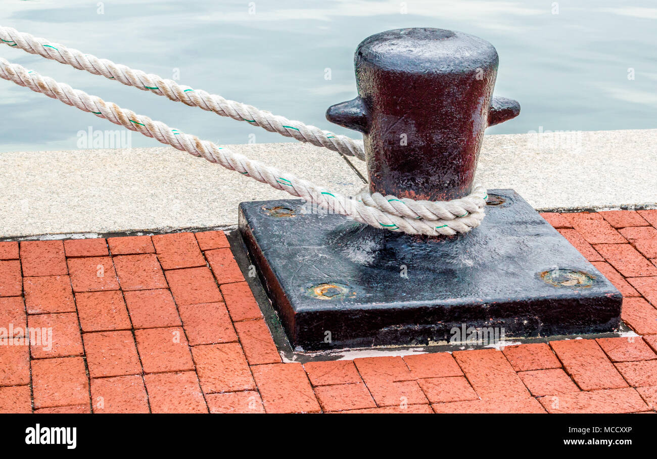 weathered black iron ships bollard with taut mooring line on a red