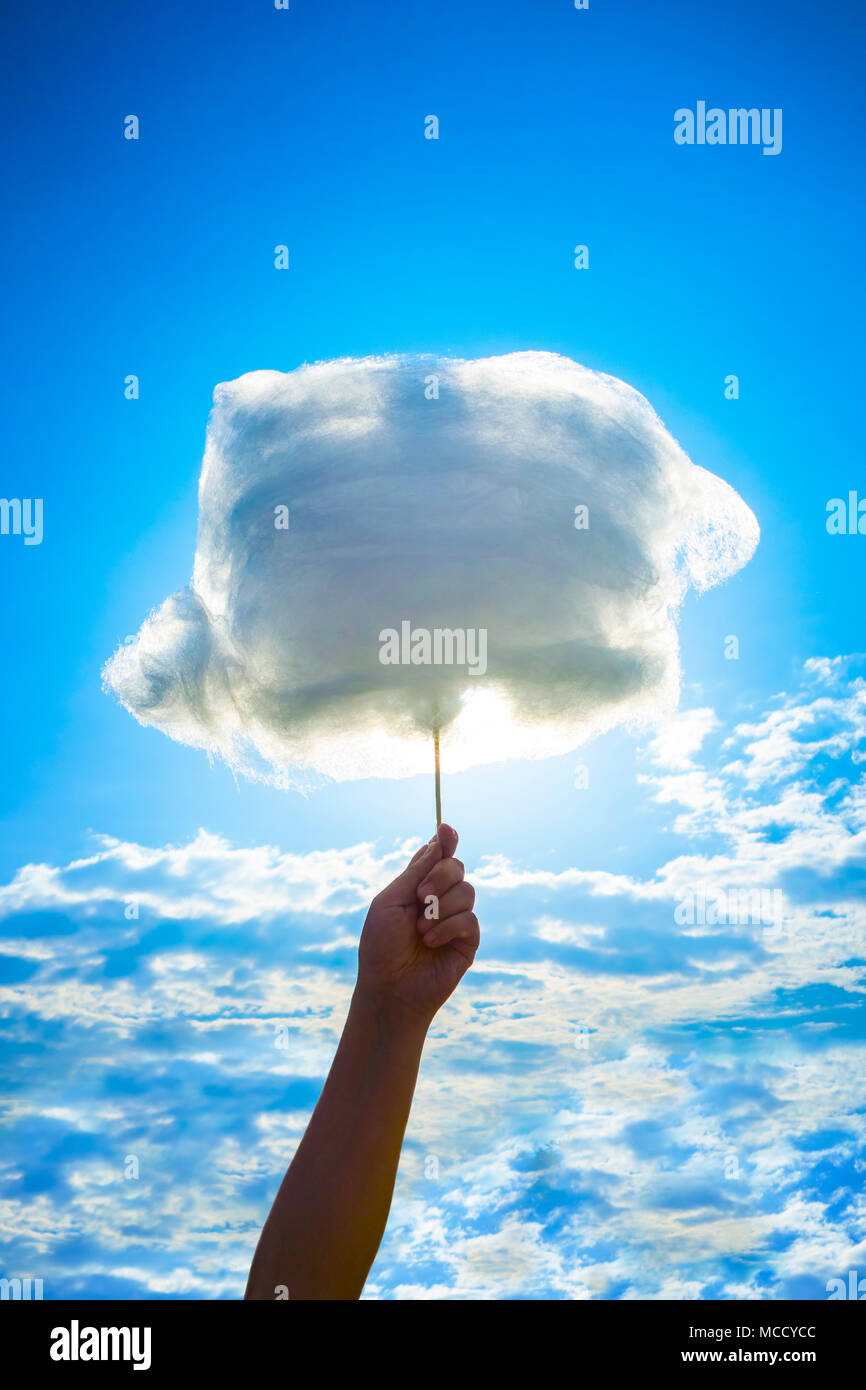 Holding Sweet Cotton Candy on Stick on Blue Cloudy Sky Background. Stock Photo