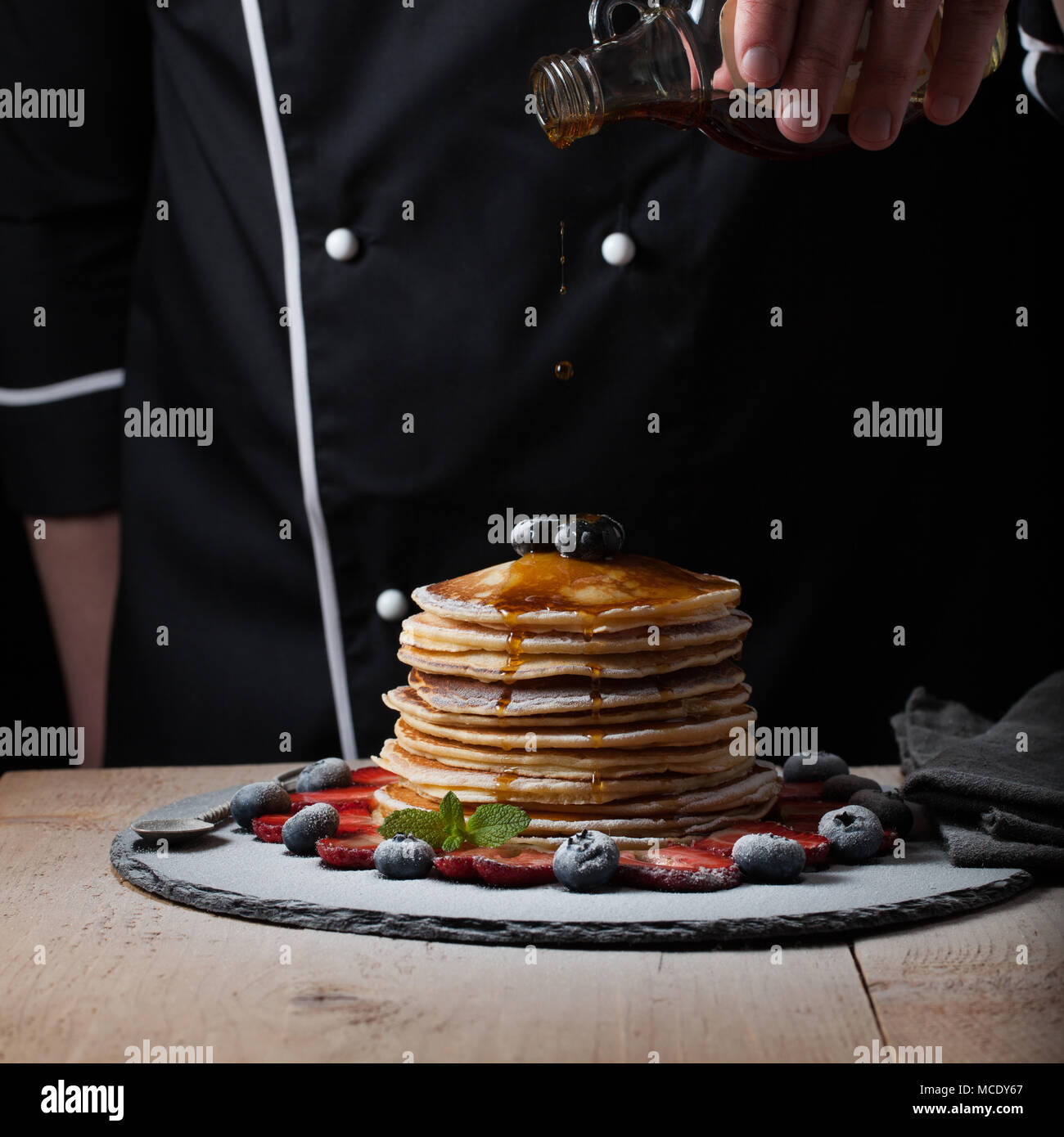 The chef pours maple syrup on pancake stack with blueberries and ...