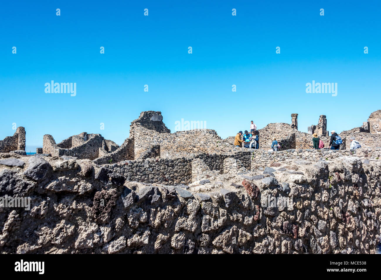 Tourists explore a section of Pompeii city ruins facing the Mediterranean, above the original  port, when the sea was once much closer; exposed walls. Stock Photo