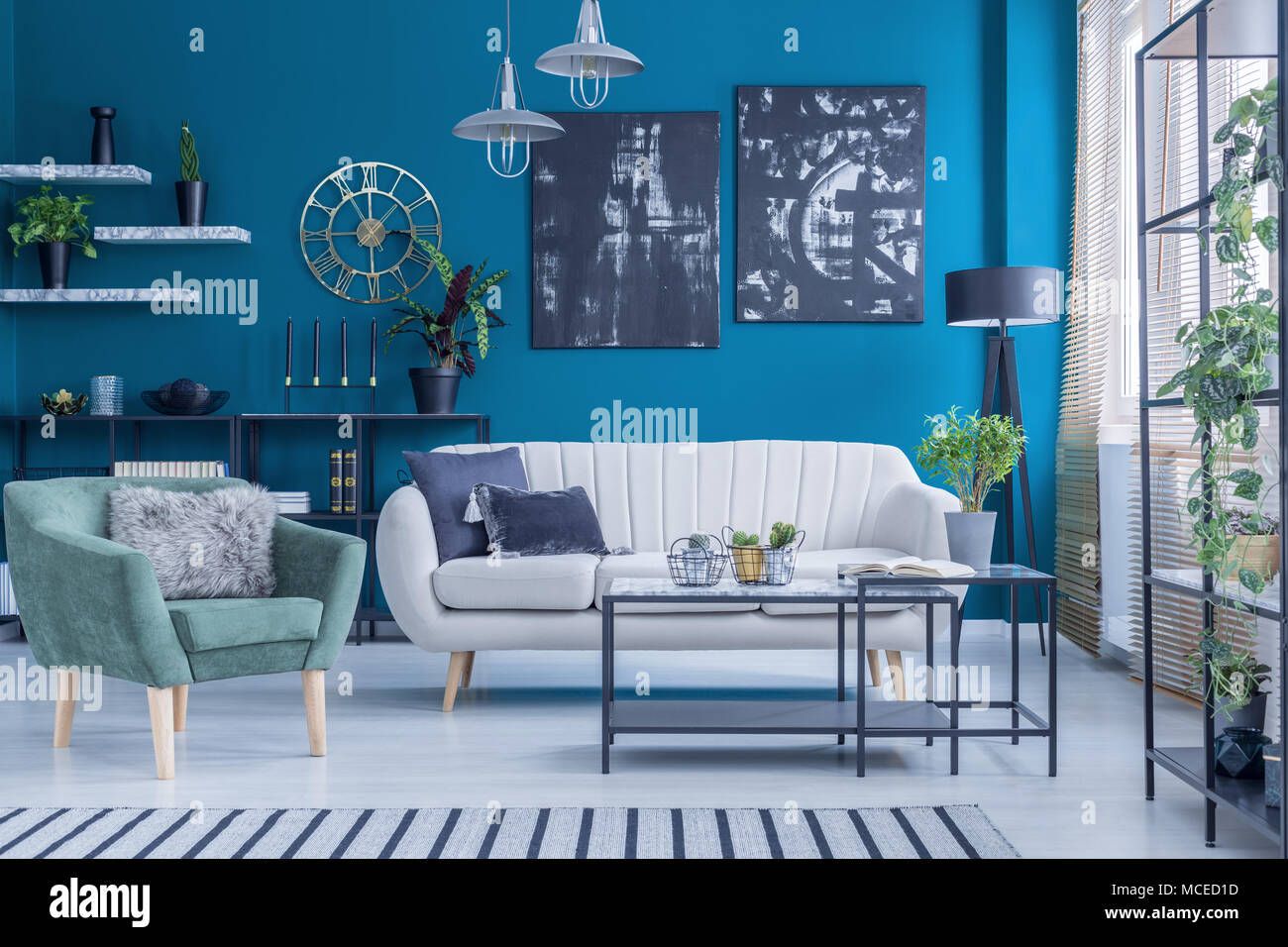 Beige sofa and green armchair against blue wall with black paintings in