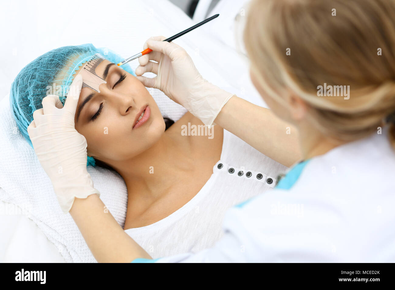 Professional beautician is going to correct eyebrow line at woman face ...