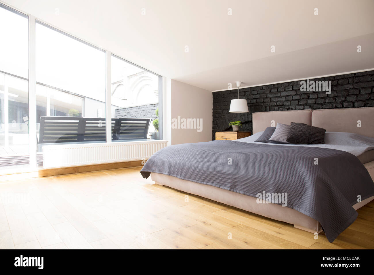 Grey bedding on bed in bright bedroom interior with windows and wooden