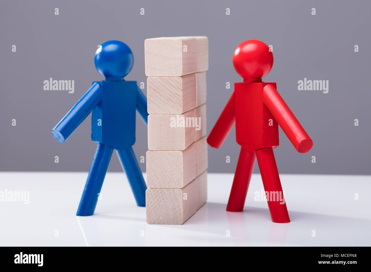 Red And Blue Human Figures Separated By Wooden Blocks Against Grey Background Stock Photo