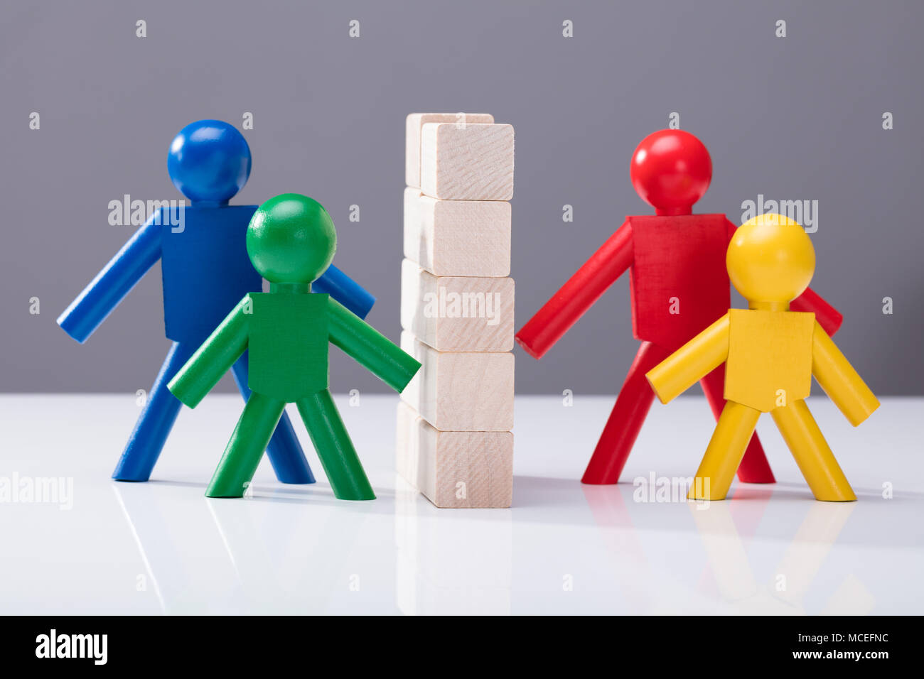 Close-up Of Multi Colored Human Figures Separated By Stacked Wooden Blocks Against Grey Background Stock Photo