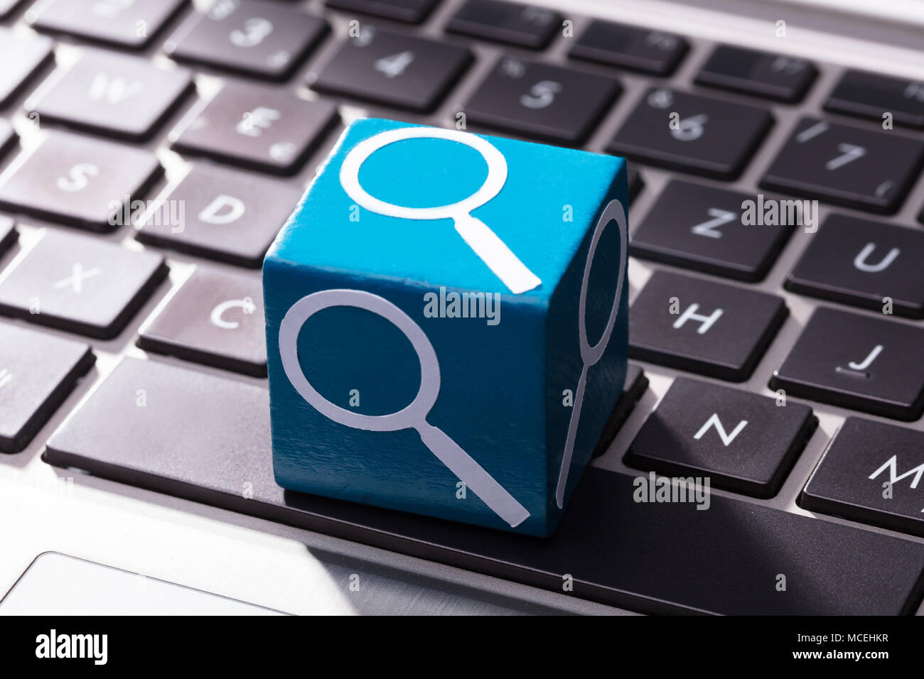 Close-up Of Magnifying Glass Symbol On Blue Wooden Block Over The Laptop  Keypad Stock Photo - Alamy