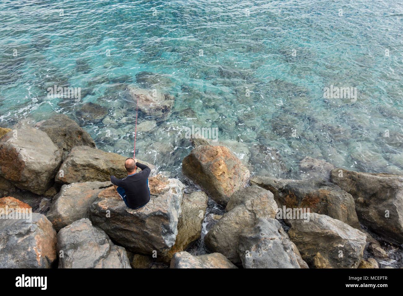 Man fishing from a rocky coastline Stock Photo