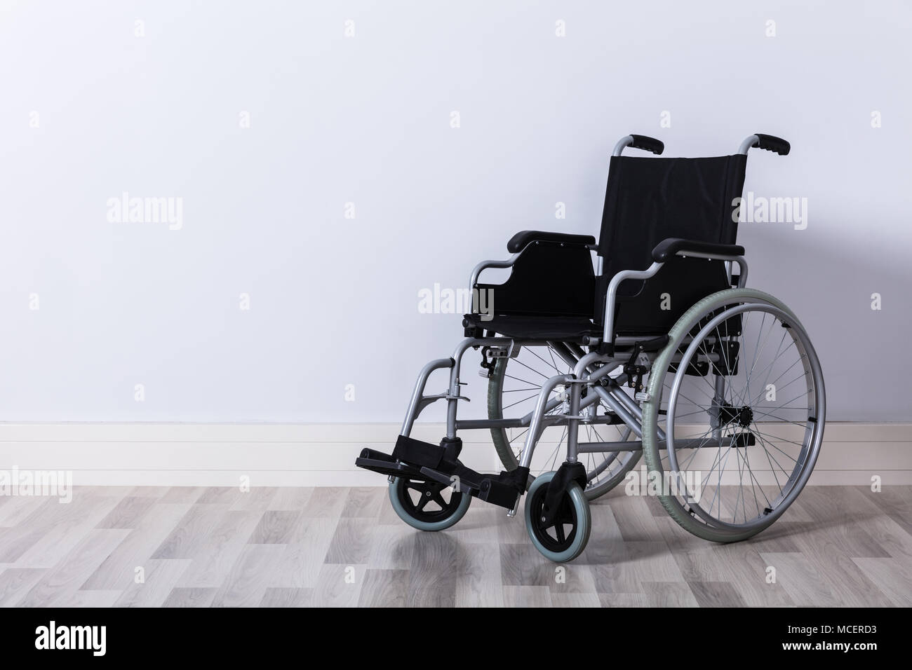 Black Colored Empty Wheelchair In Front Of Wall Stock Photo