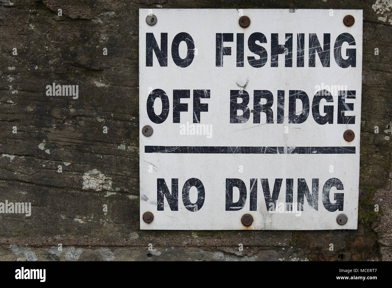 Old weathered No fishing off bridge No diving sign screwed on to old stone wall Stock Photo
