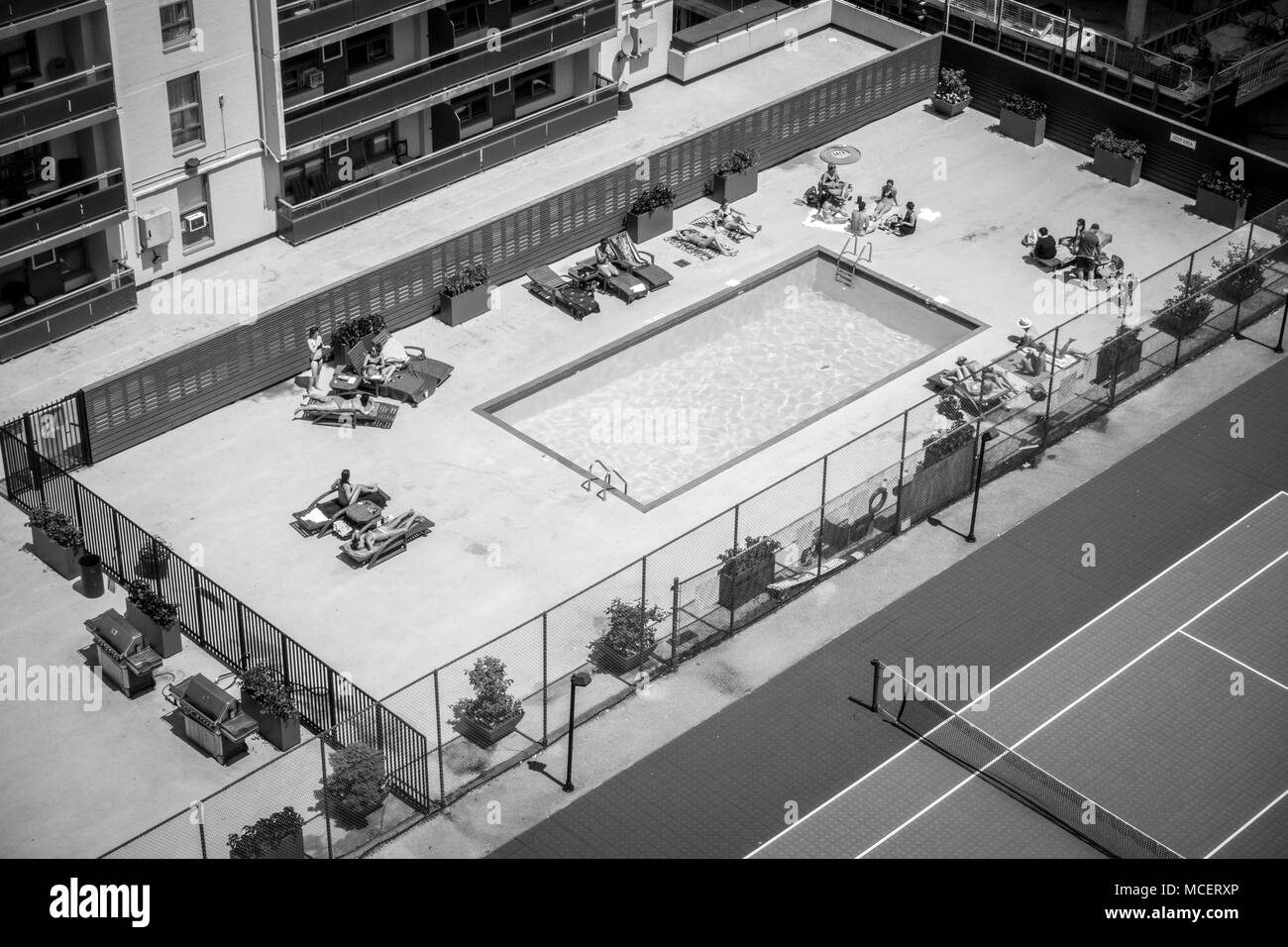 People relaxing by swimming pool next to tennis court, Toronto, Canada Stock Photo