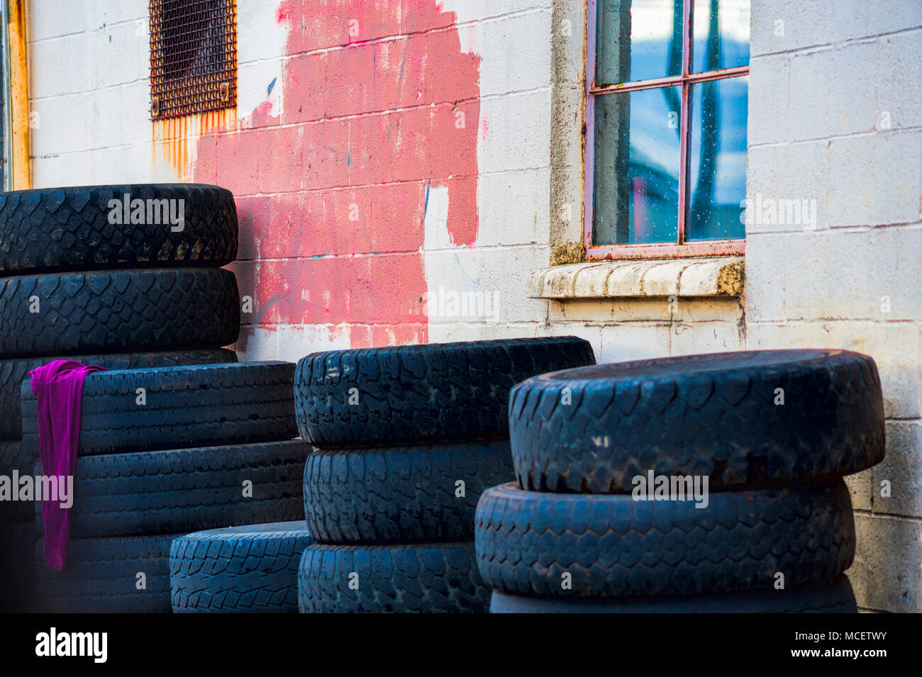 Tires stacked against a building with a red rag hanging off of one stak. Stock Photo