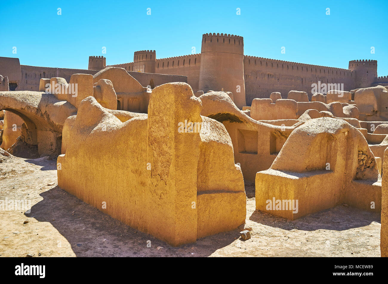 Preserved foundations and walls of ancient adbe buildings of Arg-e Rayen with massive ramparts and towers of castle on the background, Iran. Stock Photo