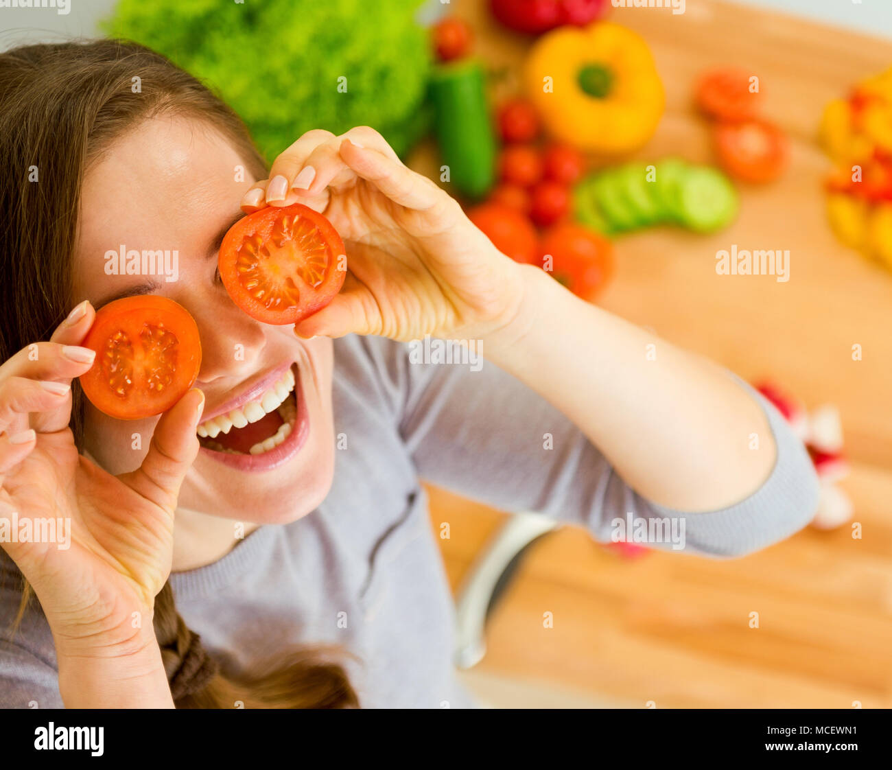 Smiling young woman holding cherry tomatos in front of face Stock Photo ...