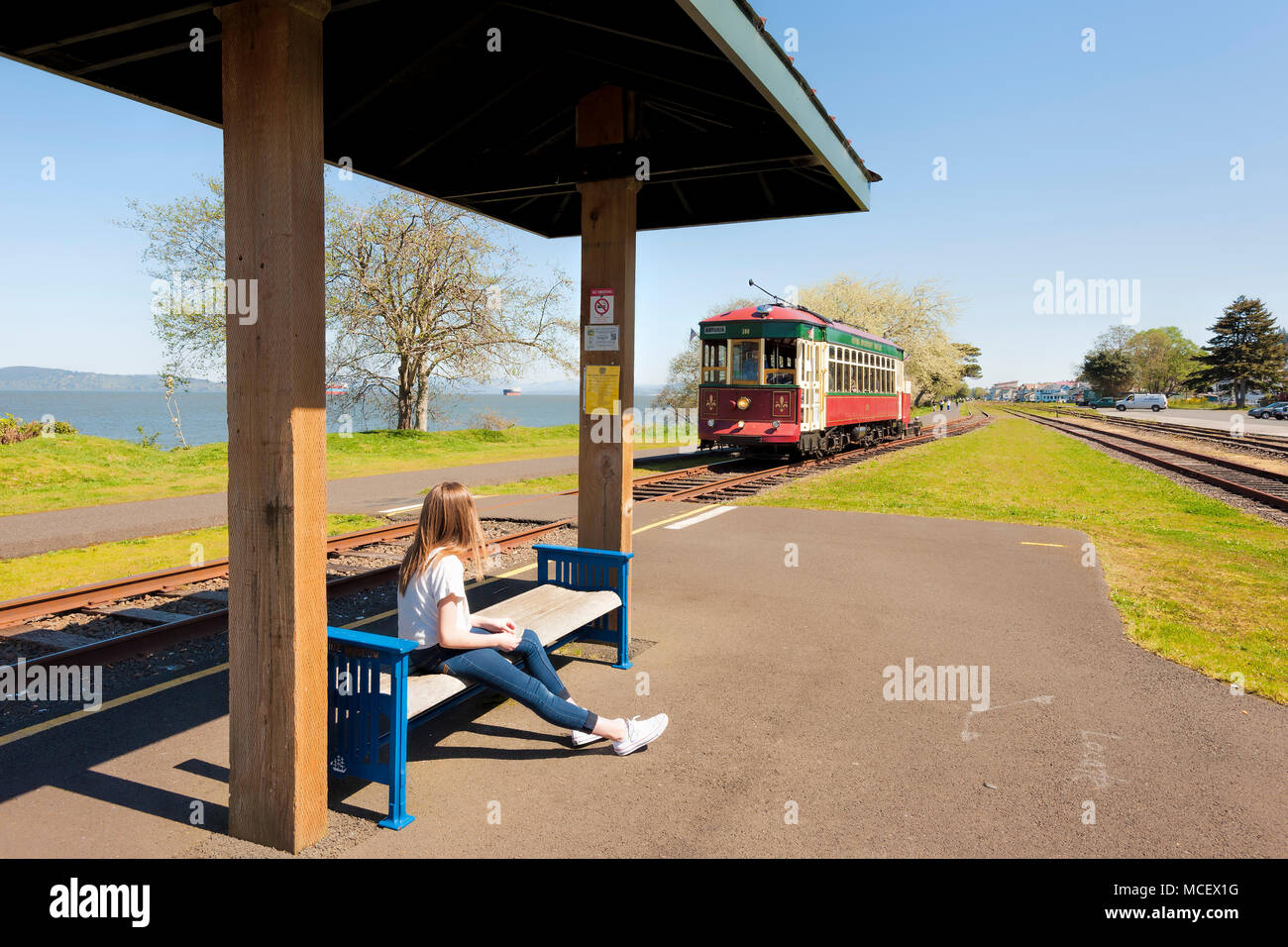 Astoria, Oregon, USA - April 7, 2016: A young girl waits at a stop to ride the trolley along the Columbia River on Astoria, Oregon's waterfront, Stock Photo