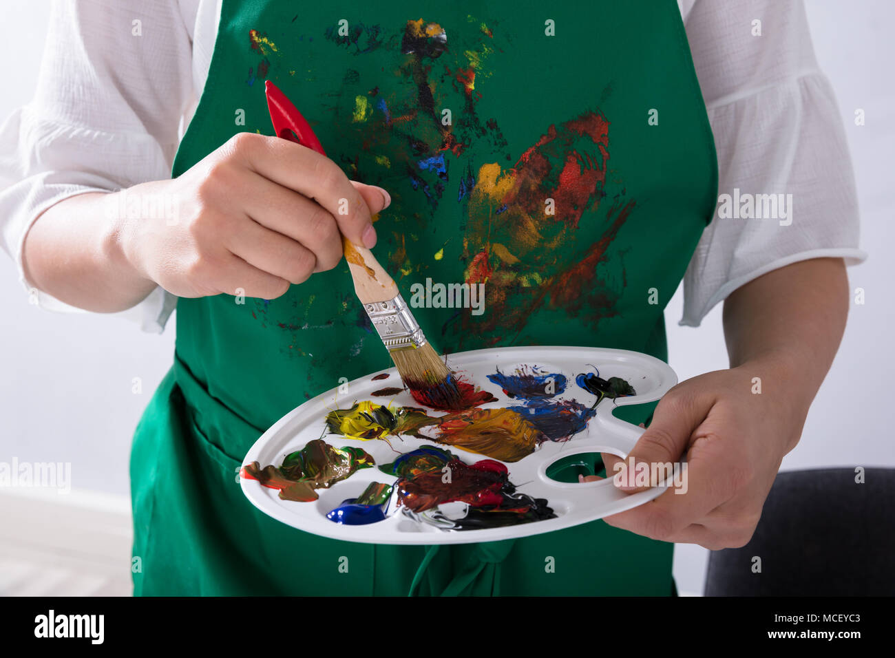 Mid Section View Of An Female Artist's Hand Holding Paint Palette And Paintbrush Stock Photo