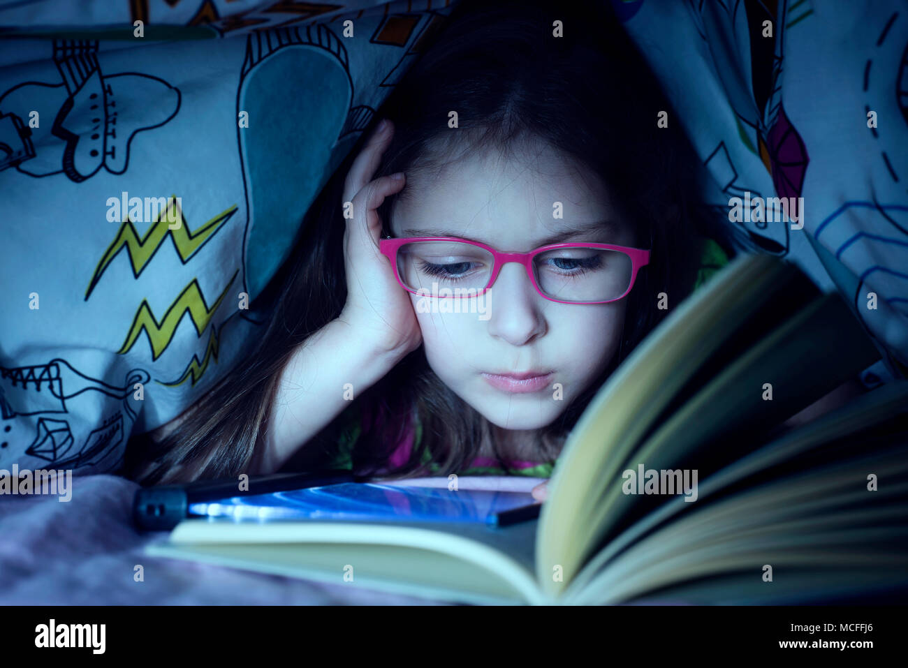 Little caucasian girl reading by stealth a book in the night under coverlet Stock Photo