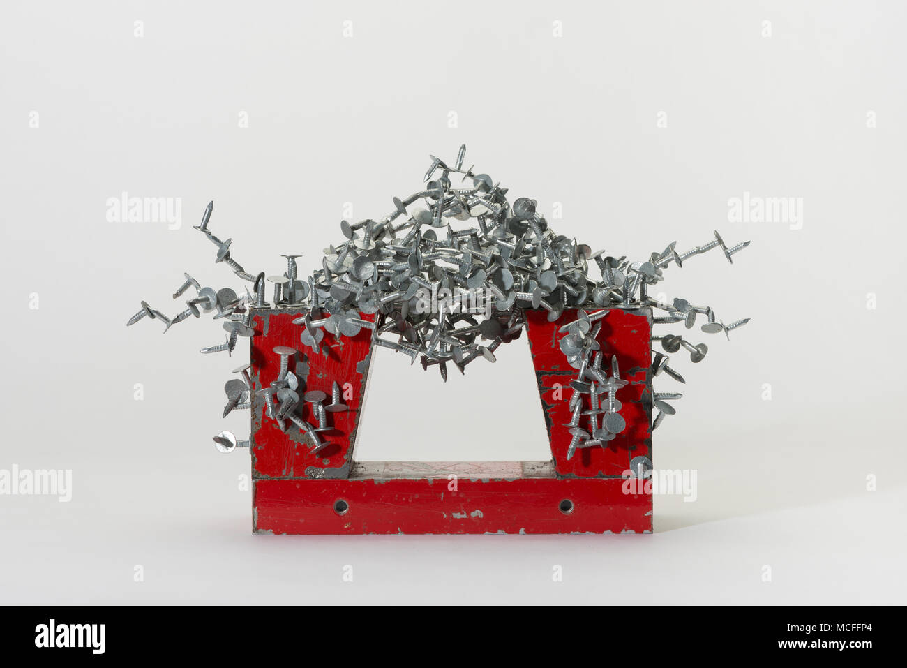 Large industrial powerful horseshoe magnet made from component parts attracting iron nails, galvanised staples, clouts demonstrating magnetic field Stock Photo
