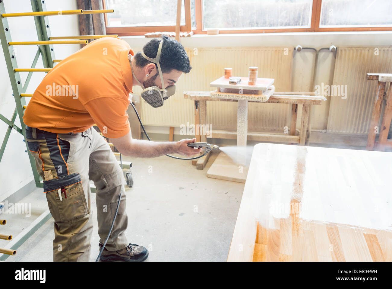 carpenter man spraying varnish on a table he works on Stock Photo